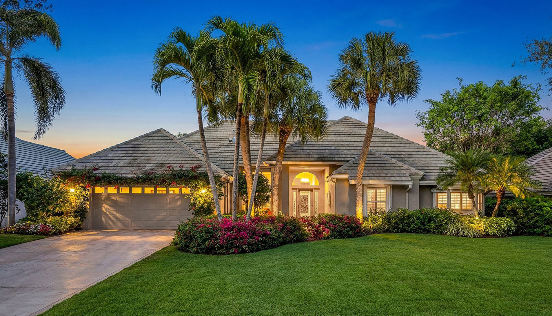 Single-story home with palm trees and lush landscaping at dusk