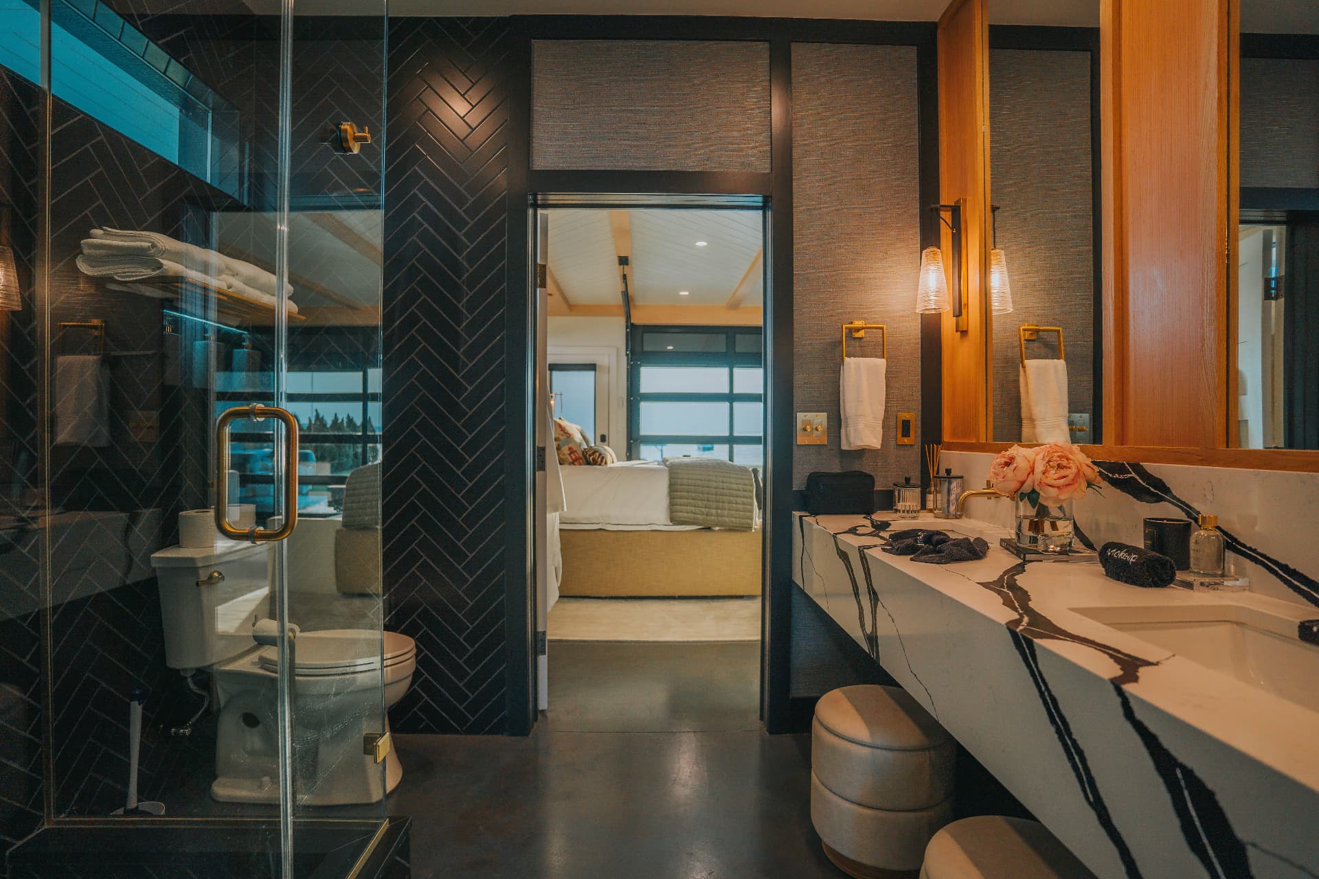Spa-style bathroom with dark herringbone tile, brass fittings, and a marble double vanity