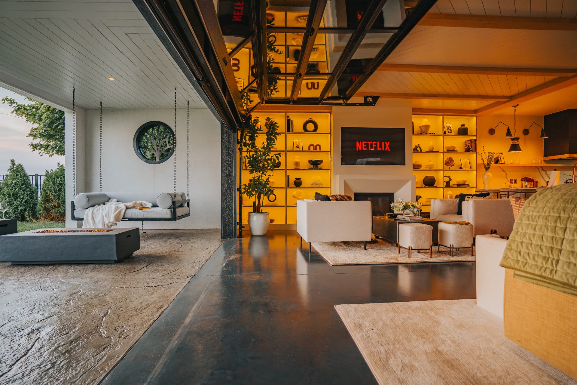 Glass wall raised to connect the living room with the covered terrace, fire table, and hanging daybed